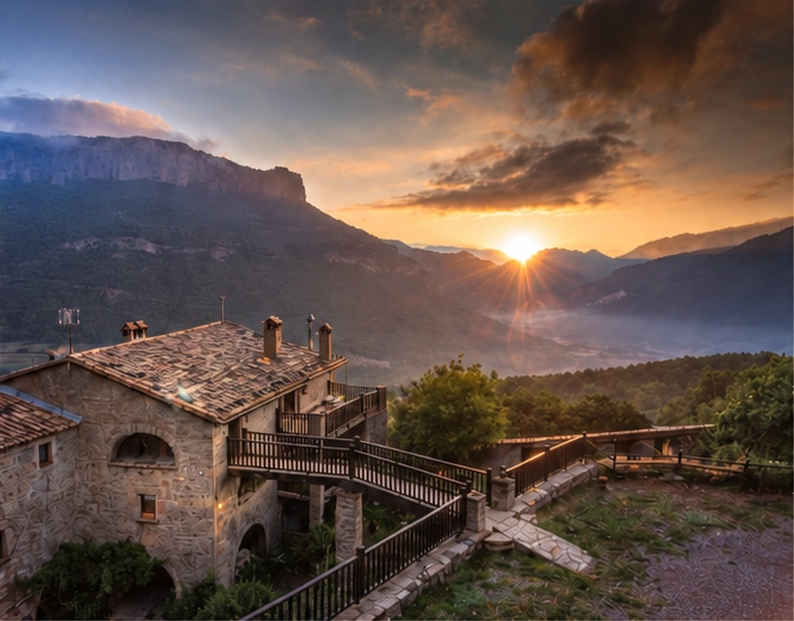 Vista de la masia Casafont i els cingles de Busa amb el sol baix a l’horitzó.